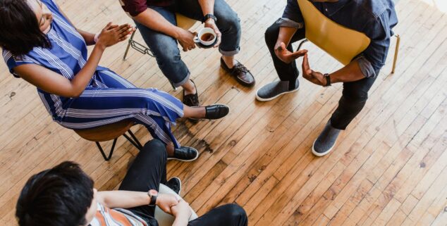 People seated in a circle of chairs talking together in a peer support group